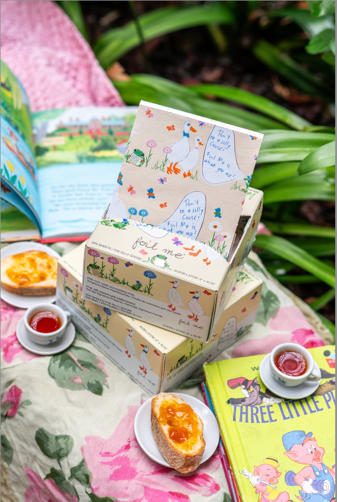 Foil Me "The Silly Goose" pre-cut hair colouring foil, 500 sheets — cream box with illustrated geese design, shown on floral fabric in a garden with tea and toast.